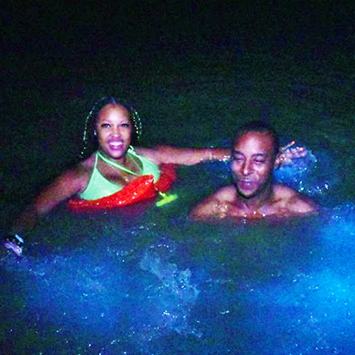 couple swims in blue glowing water at night