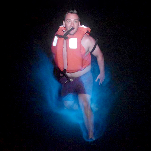 man jumps in blue glowing water at night