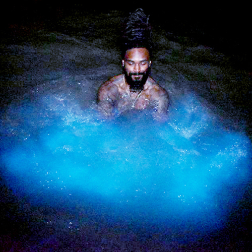 man swims in blue glowing water at night