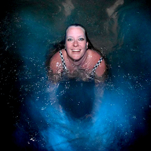 woman swims in blue glowing water at night